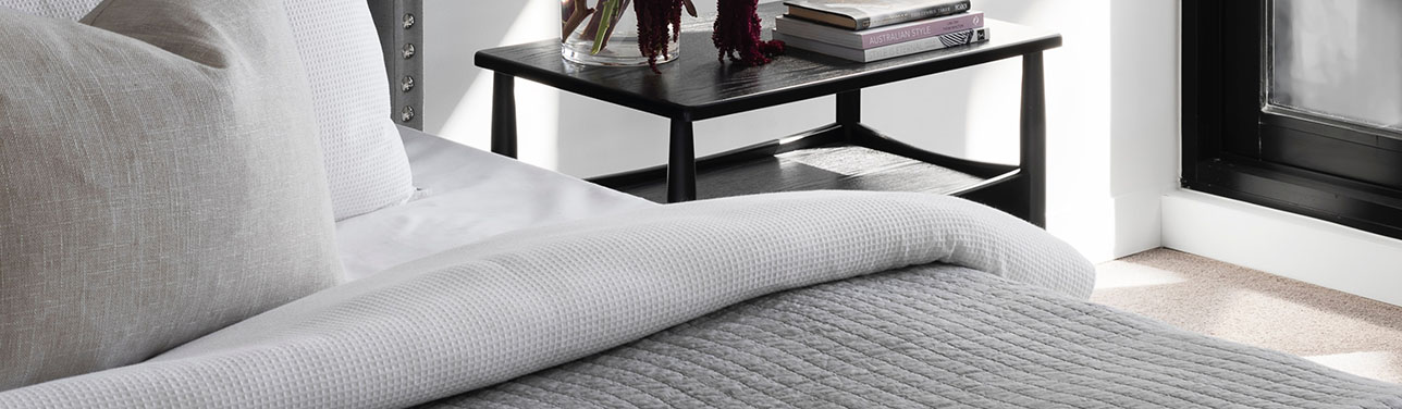 Bed with plush grey bedding and bedside table with books.