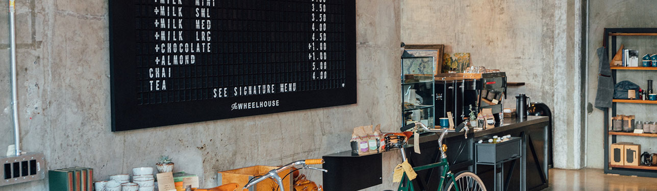 Coffee shop with large board, shelves with products, and parked bicycles.
