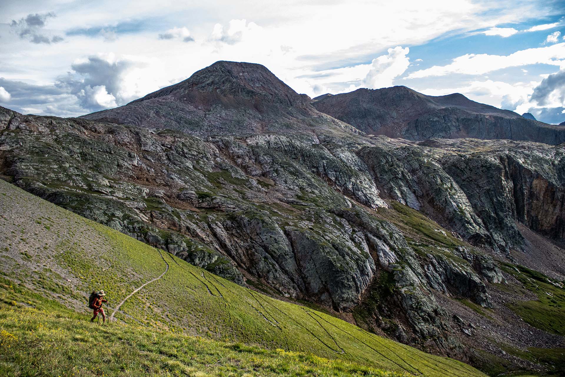 Person hiking on trail along high mountain ridge.